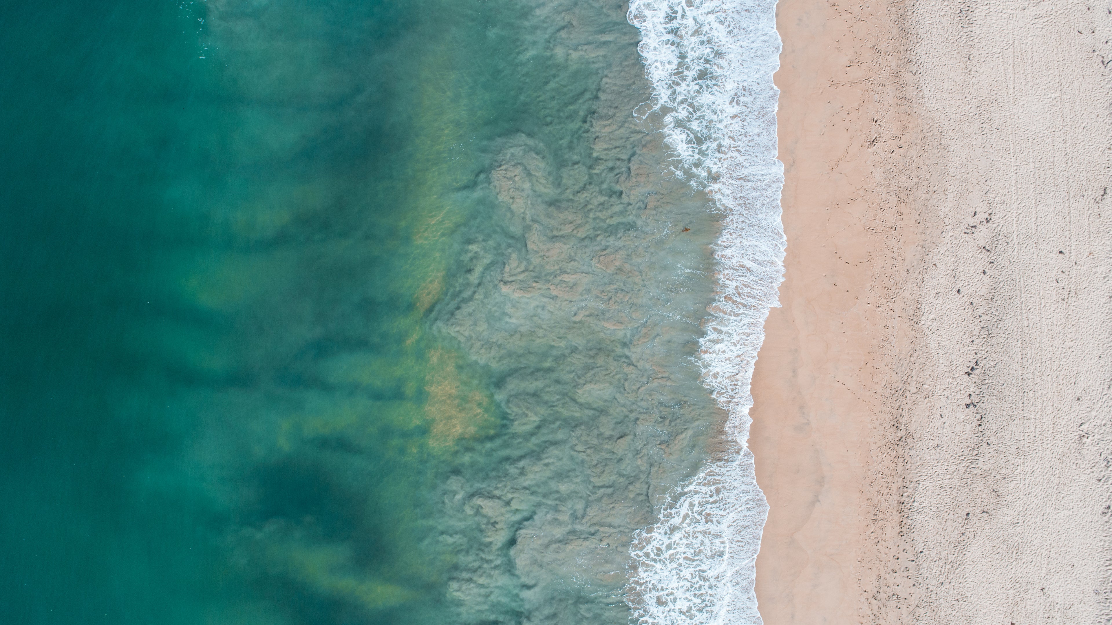 Top-down view of a beach with turquoise water and white waves.